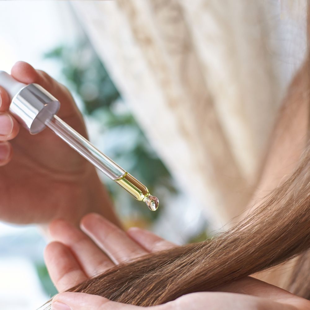 Person applying hair oil from a dropper to their hair.