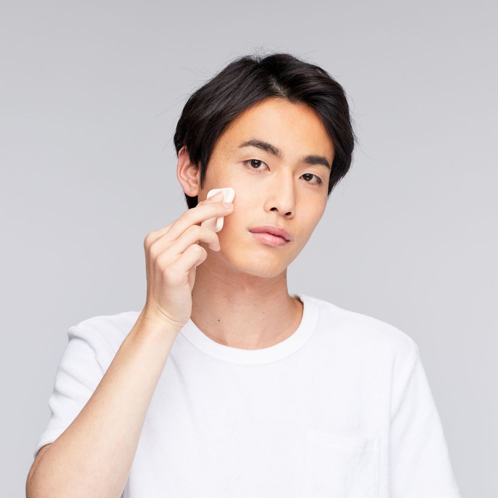 Person applying cream to face against a gray background