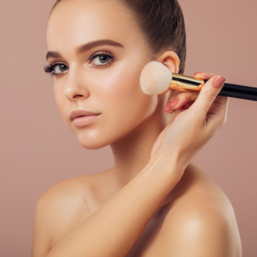 Woman applying makeup with a brush on a beige background